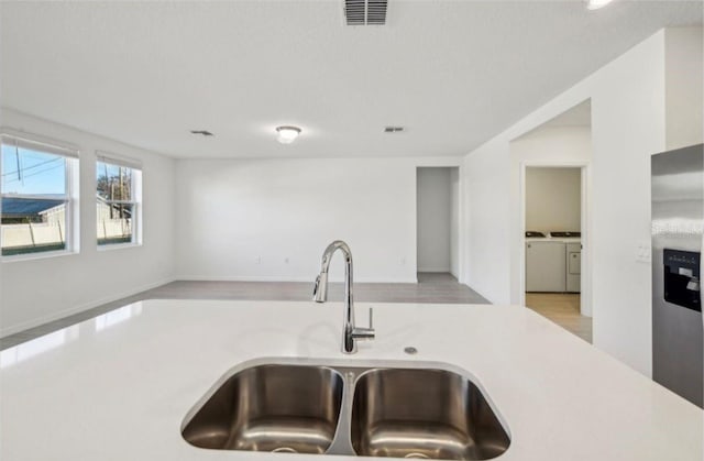 kitchen with stainless steel fridge, sink, washer and dryer, and light wood-type flooring