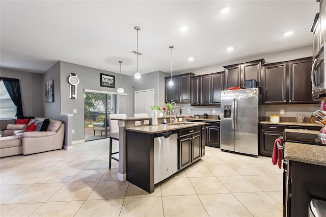 kitchen featuring appliances with stainless steel finishes, an island with sink, sink, hanging light fixtures, and light stone countertops