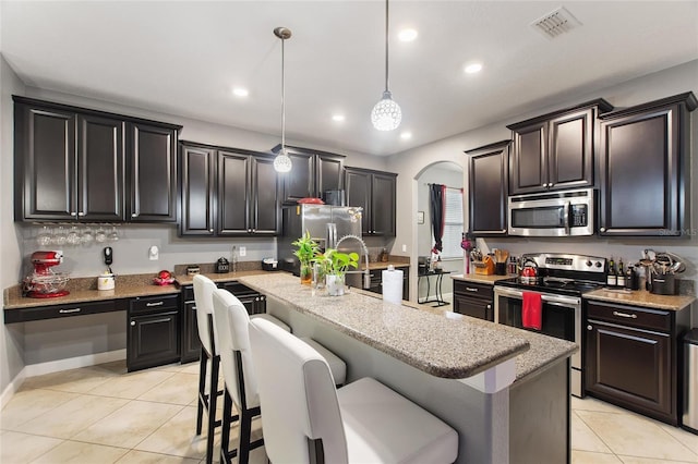 kitchen featuring appliances with stainless steel finishes, a kitchen breakfast bar, a kitchen island with sink, and hanging light fixtures