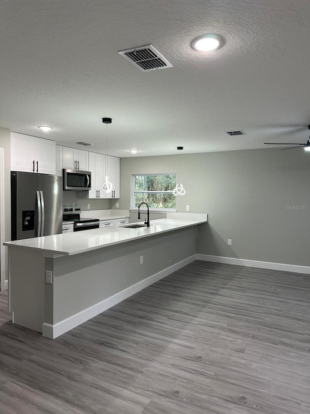 kitchen featuring stainless steel appliances, kitchen peninsula, hanging light fixtures, and white cabinets