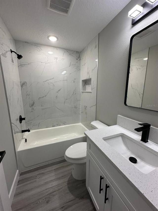 full bathroom featuring tiled shower / bath, hardwood / wood-style floors, vanity, toilet, and a textured ceiling