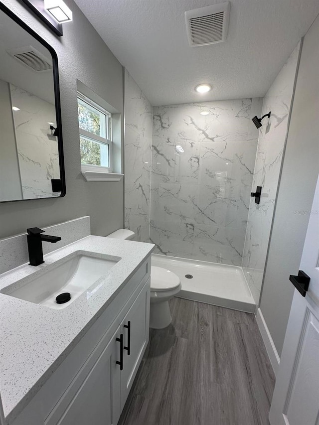 bathroom with hardwood / wood-style floors, a tile shower, vanity, a textured ceiling, and toilet