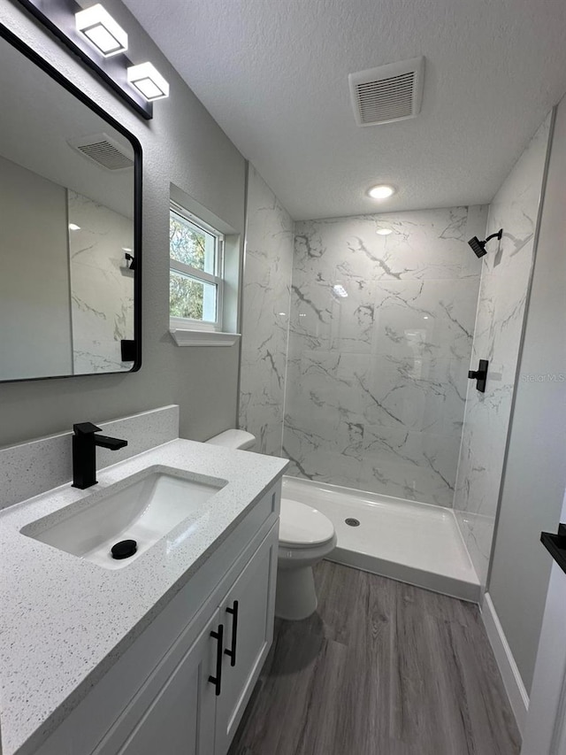 bathroom with hardwood / wood-style flooring, vanity, a tile shower, a textured ceiling, and toilet