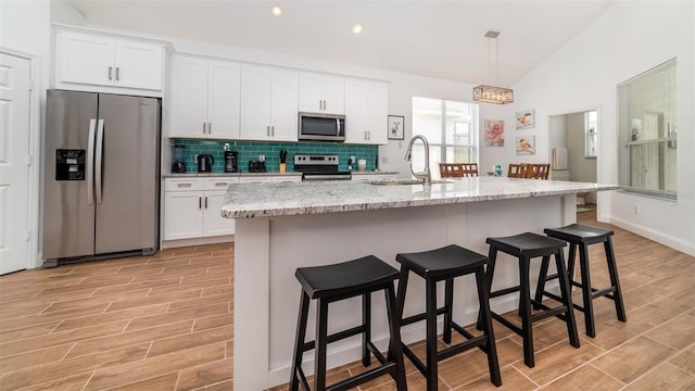 kitchen with a kitchen bar, sink, appliances with stainless steel finishes, an island with sink, and white cabinets