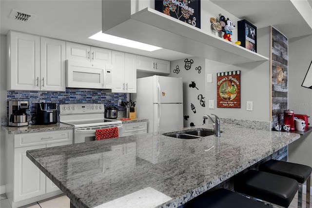 kitchen featuring sink, white appliances, tasteful backsplash, a kitchen bar, and kitchen peninsula