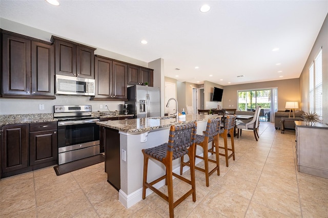 kitchen featuring appliances with stainless steel finishes, sink, a breakfast bar area, light stone counters, and a center island with sink