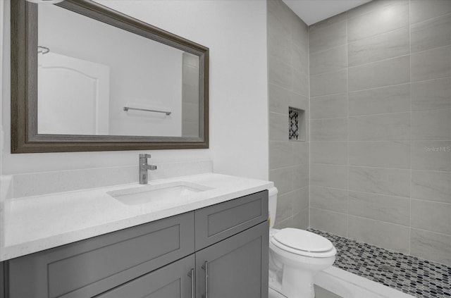 bathroom with tiled shower, vanity, and toilet