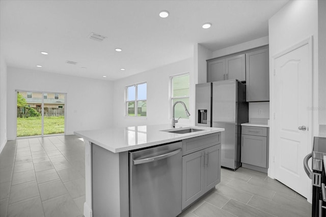 kitchen featuring stainless steel appliances, sink, gray cabinets, and an island with sink