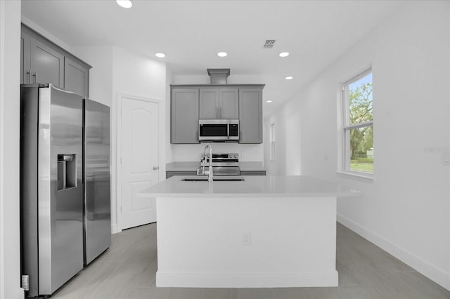 kitchen with stainless steel appliances, gray cabinets, sink, and a center island with sink