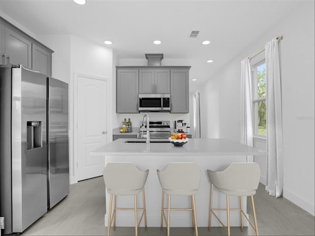 kitchen with stainless steel appliances, a kitchen island with sink, sink, and gray cabinets