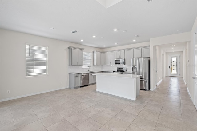 kitchen featuring sink, gray cabinets, stainless steel appliances, a kitchen island, and decorative backsplash