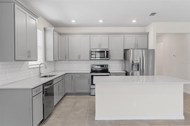 kitchen with sink, gray cabinets, backsplash, stainless steel appliances, and a kitchen island