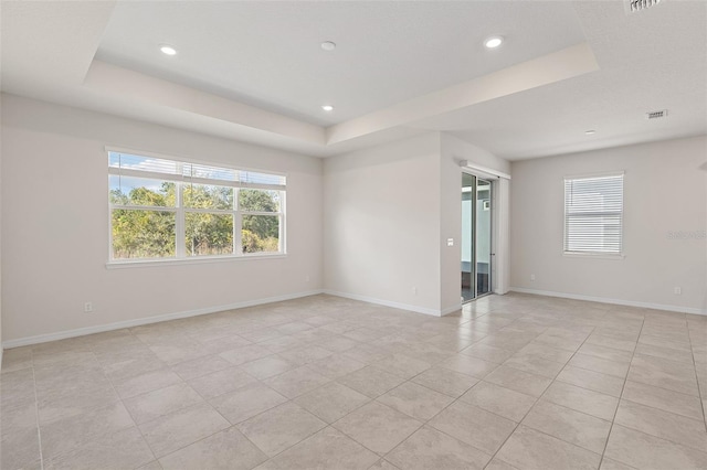 spare room with a tray ceiling, a wealth of natural light, and light tile patterned flooring