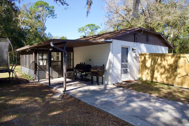 view of front of home featuring a trampoline, fence, a sunroom, concrete block siding, and a patio area