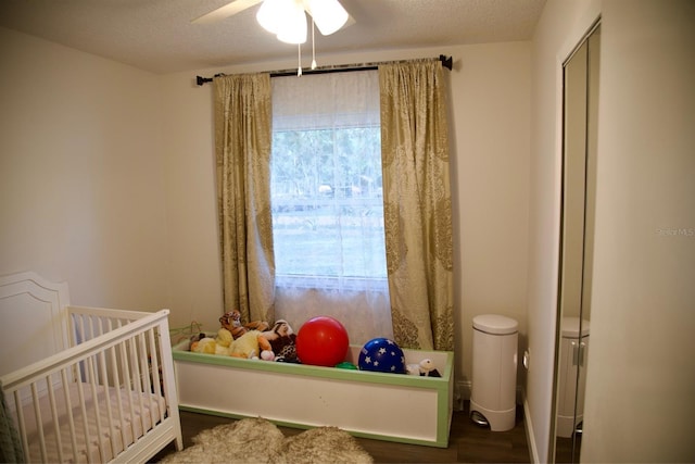 bedroom featuring a nursery area, dark wood-type flooring, a textured ceiling, and ceiling fan