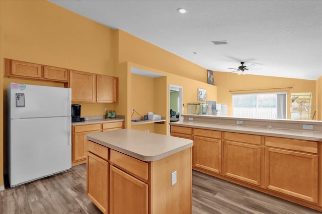 kitchen featuring white refrigerator, a textured ceiling, a kitchen island, vaulted ceiling, and light wood-type flooring