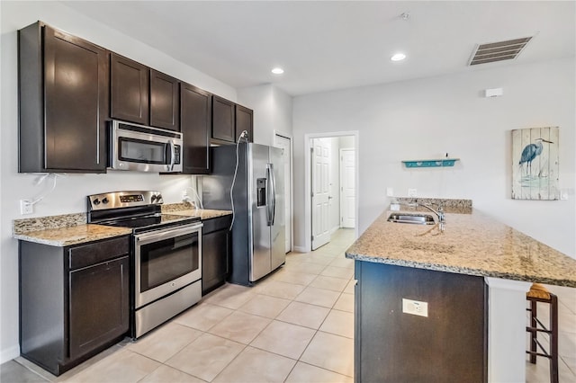 kitchen featuring a kitchen bar, sink, dark brown cabinets, kitchen peninsula, and stainless steel appliances