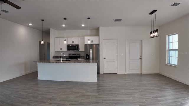 kitchen featuring white cabinetry, sink, dark stone countertops, hanging light fixtures, and stainless steel appliances