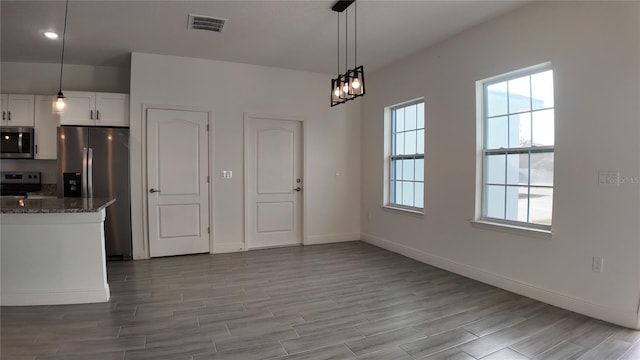 kitchen featuring white cabinetry, stainless steel appliances, decorative light fixtures, and dark stone countertops