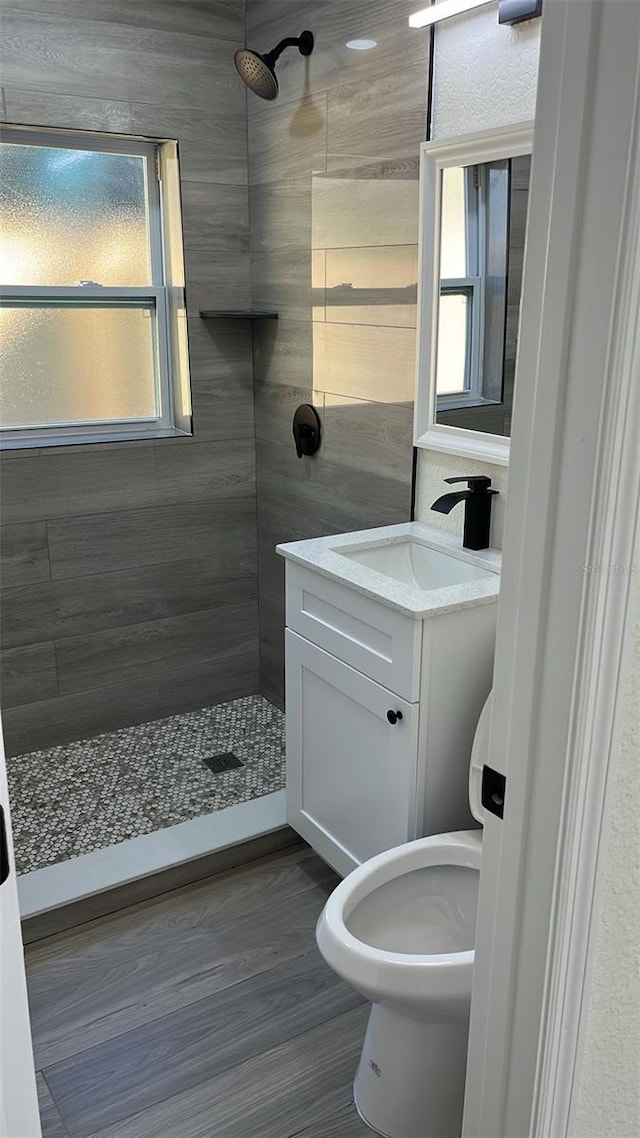 bathroom with vanity, tiled shower, hardwood / wood-style floors, and toilet