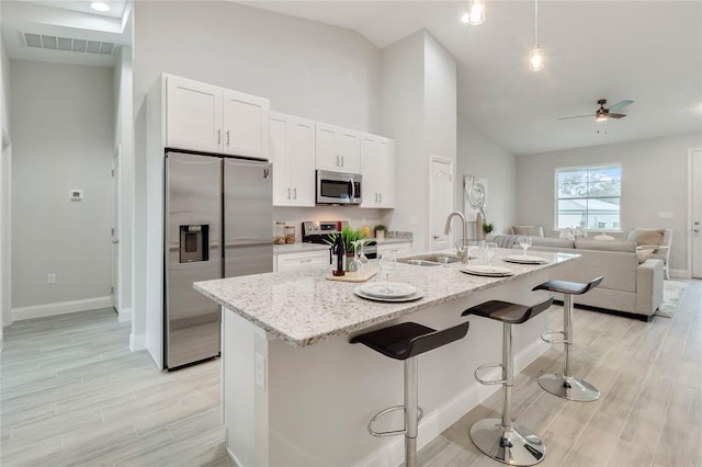 kitchen with sink, a kitchen breakfast bar, an island with sink, stainless steel appliances, and white cabinets