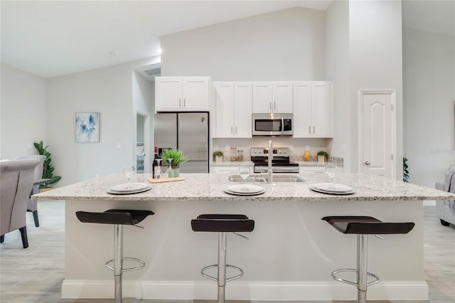 kitchen with a breakfast bar, white cabinetry, a kitchen island with sink, stainless steel appliances, and light stone countertops