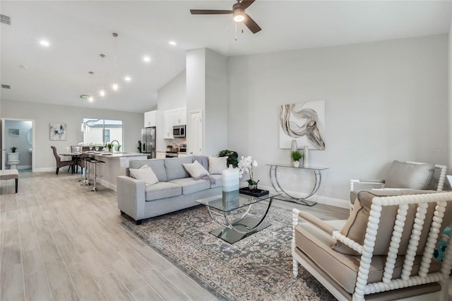 living room featuring ceiling fan, sink, high vaulted ceiling, and light wood-type flooring