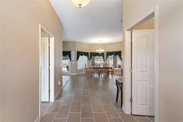 hall featuring dark tile patterned flooring and a chandelier