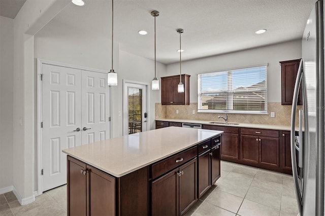 kitchen with light countertops, backsplash, freestanding refrigerator, and a sink