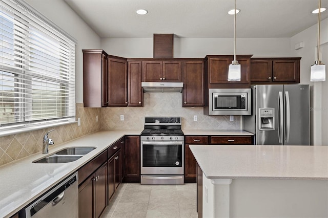 kitchen with tasteful backsplash, under cabinet range hood, appliances with stainless steel finishes, hanging light fixtures, and a sink