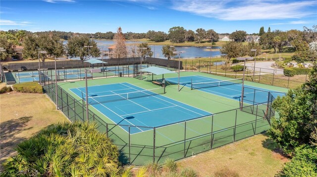 view of tennis court with a water view and fence