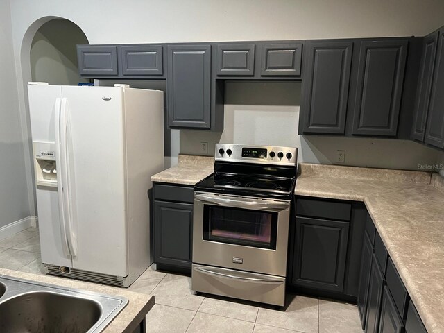 kitchen featuring white refrigerator with ice dispenser, stainless steel electric stove, gray cabinets, light countertops, and light tile patterned flooring