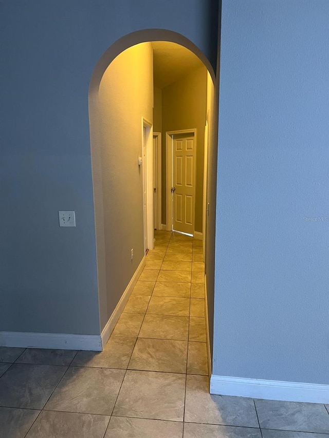 corridor with arched walkways, tile patterned floors, and baseboards