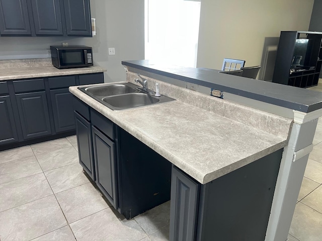 kitchen featuring black microwave, light countertops, a sink, and a center island with sink