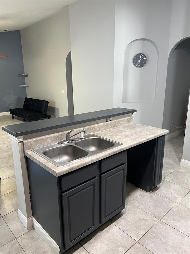 kitchen featuring arched walkways, light tile patterned flooring, a sink, baseboards, and a center island with sink