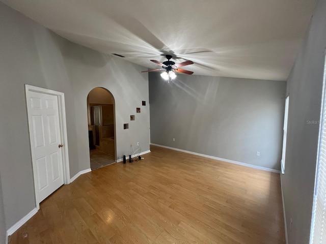 empty room with a ceiling fan, arched walkways, light wood-style flooring, and baseboards