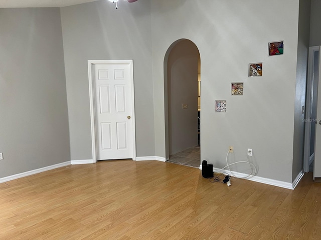 empty room featuring arched walkways, baseboards, and light wood finished floors