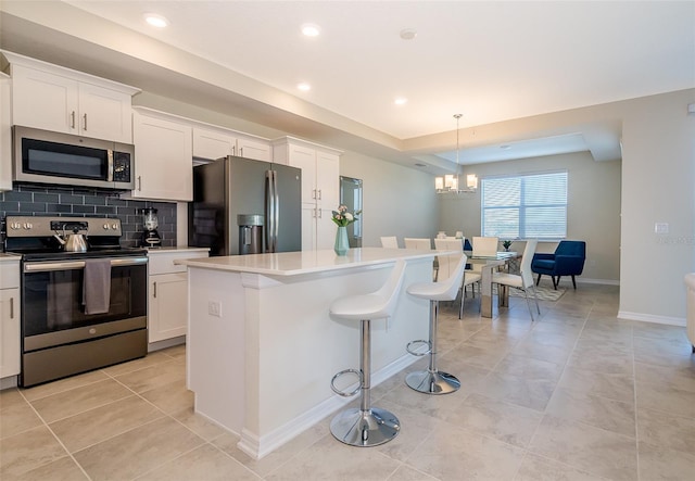 kitchen with stainless steel appliances, a kitchen island, hanging light fixtures, and white cabinetry