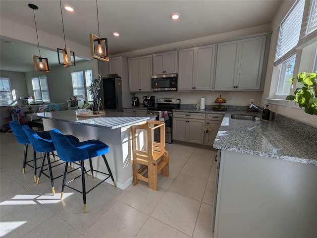 kitchen with gray cabinets, stainless steel appliances, light stone counters, a kitchen island, and decorative light fixtures