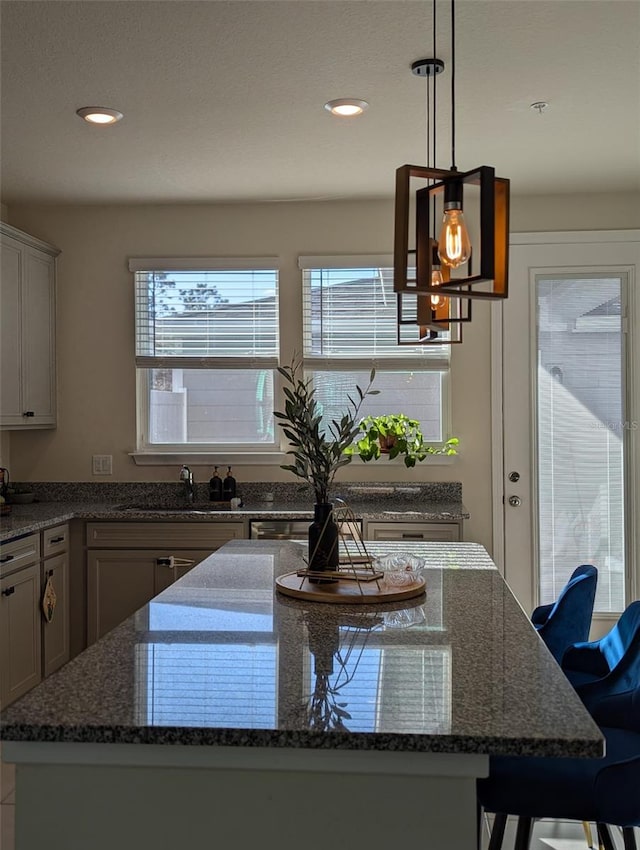 kitchen with a kitchen bar, sink, hanging light fixtures, and dark stone countertops