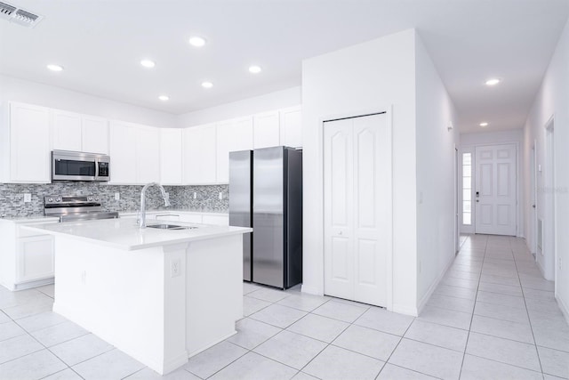 kitchen featuring sink, white cabinets, light tile patterned floors, stainless steel appliances, and a center island with sink