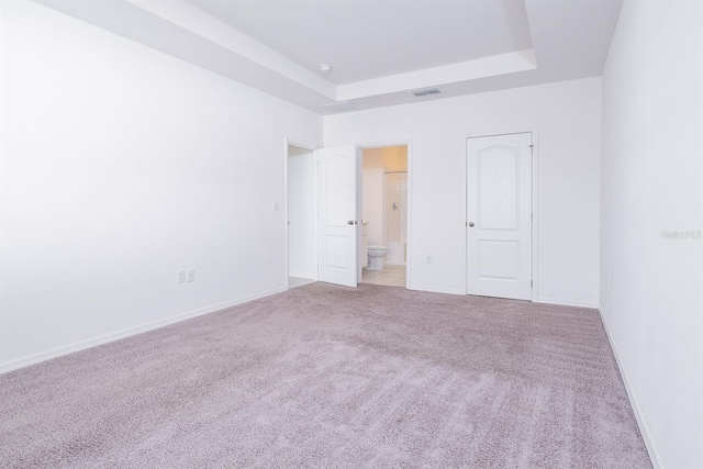 unfurnished bedroom with connected bathroom, a raised ceiling, and light carpet