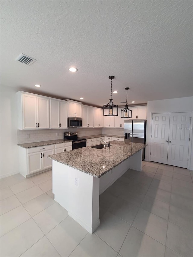 kitchen featuring decorative light fixtures, appliances with stainless steel finishes, a kitchen island with sink, and dark stone counters