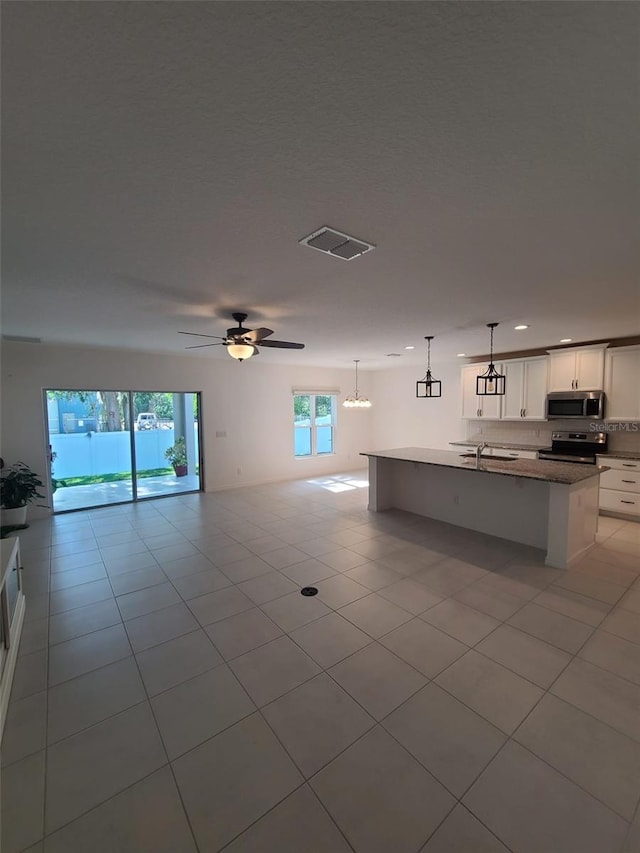 kitchen with appliances with stainless steel finishes, decorative light fixtures, white cabinetry, an island with sink, and light tile patterned floors