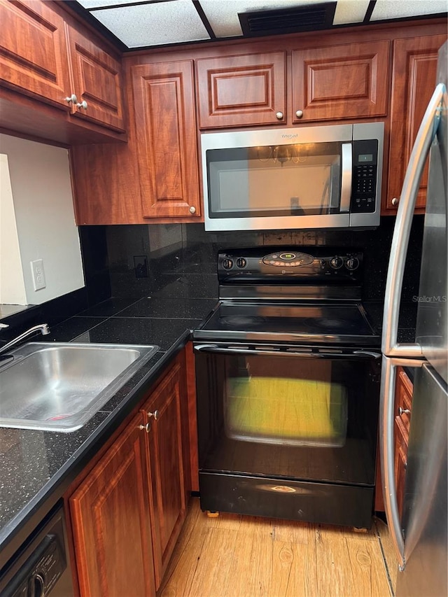 kitchen featuring sink, backsplash, dark stone counters, stainless steel appliances, and light wood-type flooring