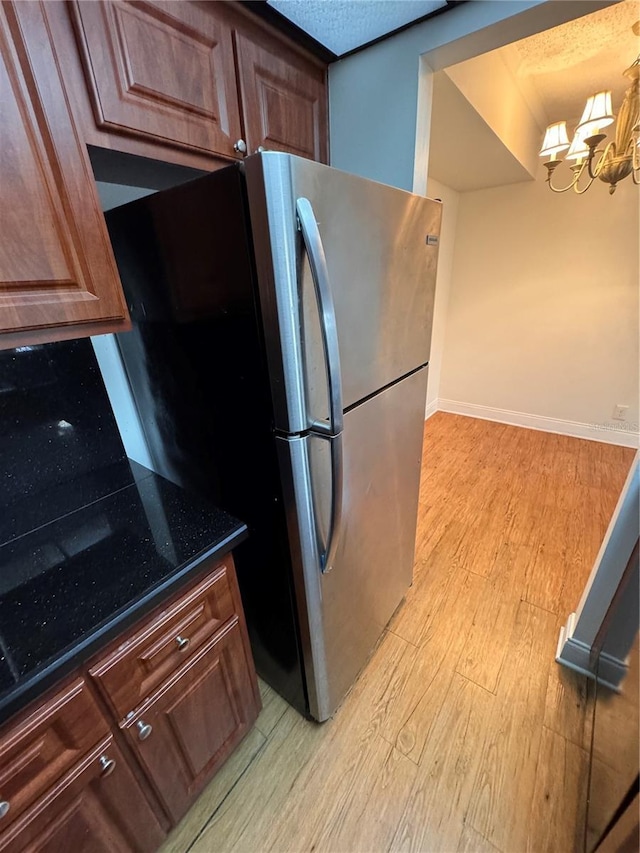 kitchen featuring a notable chandelier, light hardwood / wood-style floors, stainless steel refrigerator, and dark stone counters