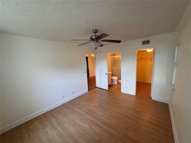 unfurnished bedroom featuring hardwood / wood-style flooring, a walk in closet, a textured ceiling, ensuite bath, and a closet