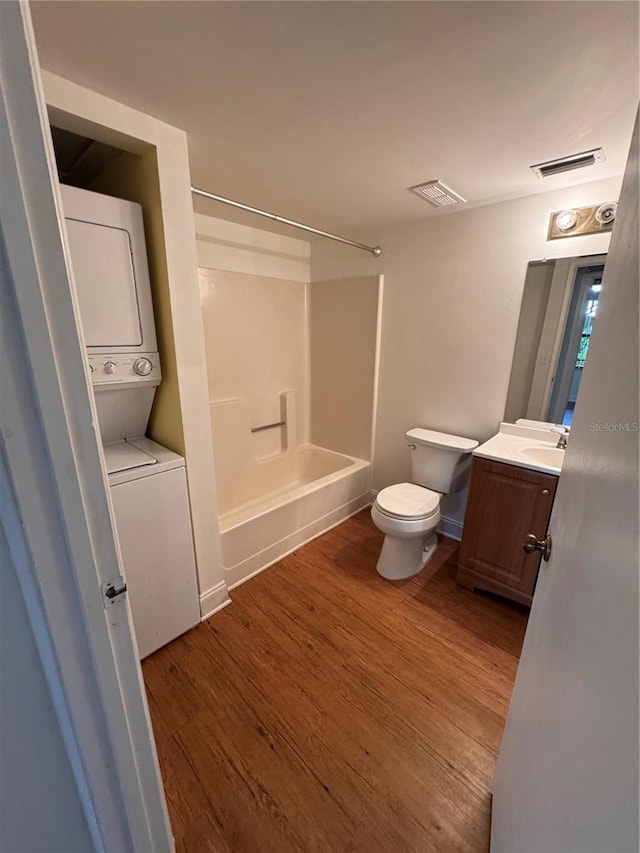 full bathroom featuring stacked washer and dryer, hardwood / wood-style flooring, vanity, shower / bathtub combination, and toilet