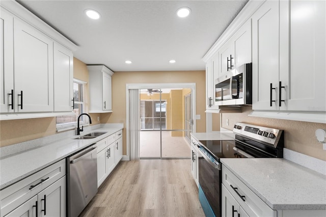 kitchen with sink, appliances with stainless steel finishes, white cabinetry, light stone counters, and light wood-type flooring