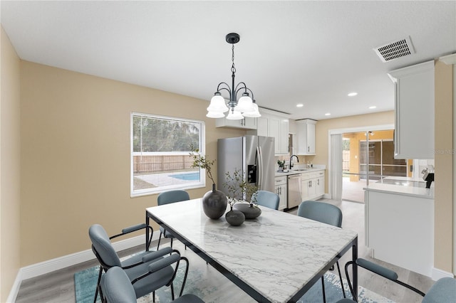 dining area featuring an inviting chandelier, sink, and light hardwood / wood-style flooring